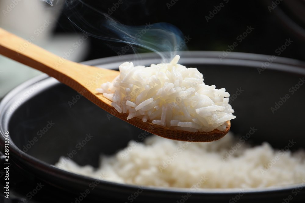 Spoon with tasty hot rice over cooker, closeup